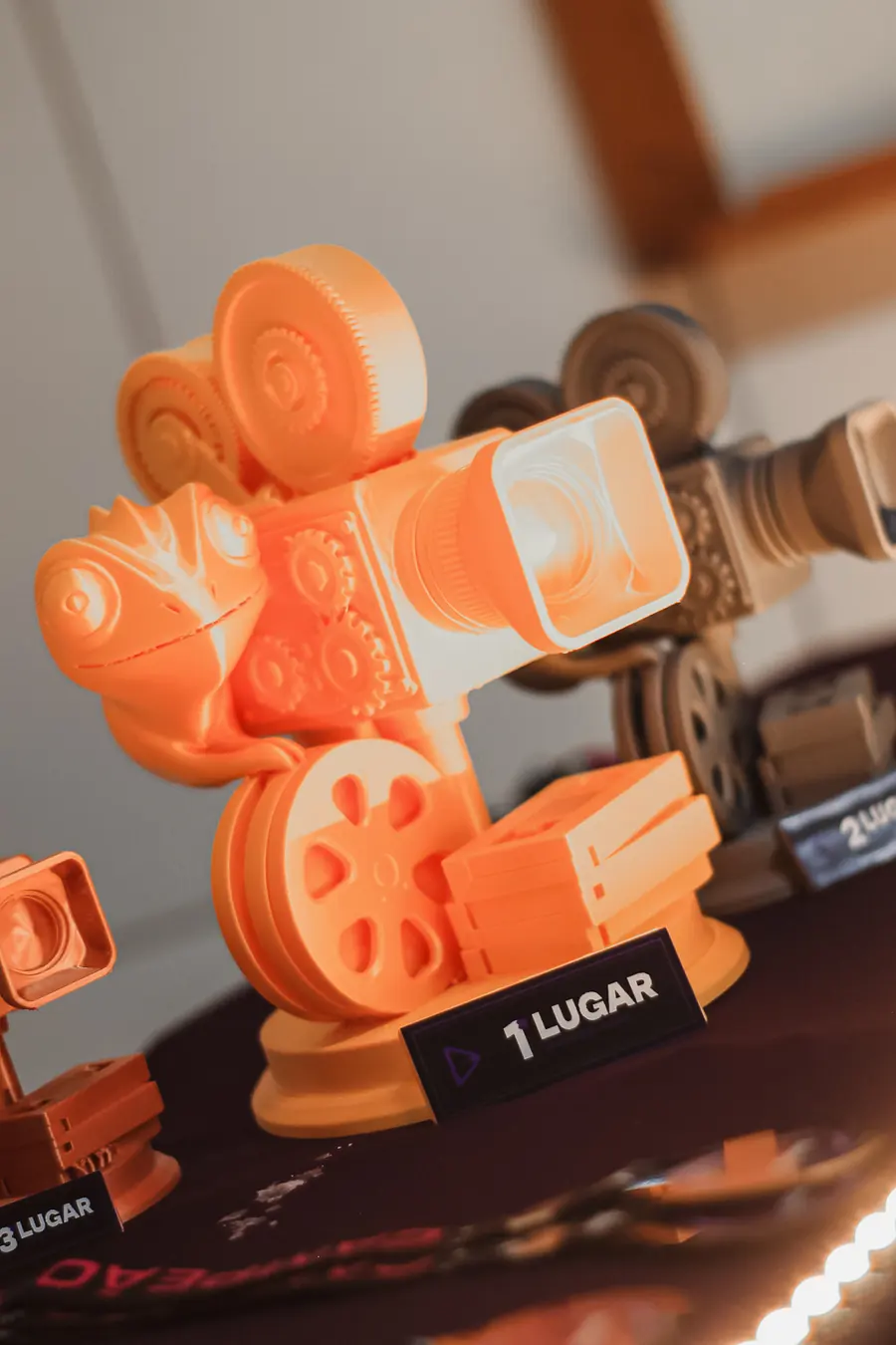 O troféu de primeiro lugar: uma câmera de cinema laranja com olhos de camaleão, sobre a mesa dos prêmios.