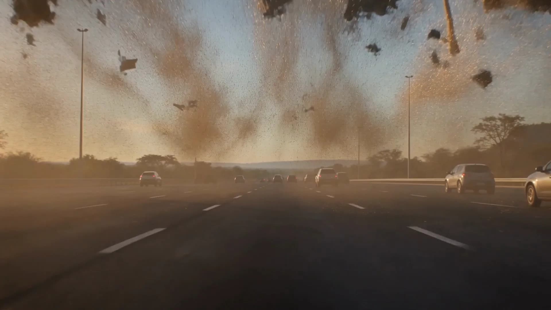 Quadro do filme: poeira e destroços da praça de pedágio sobre a rodovia, ao entardecer.