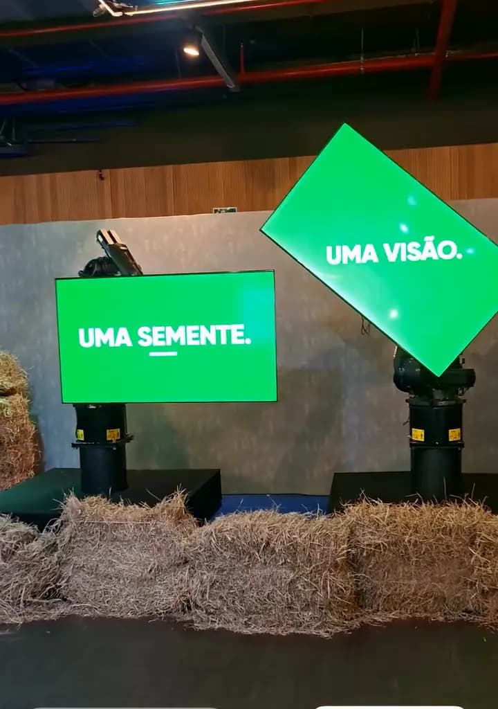 Registro do evento: dois monitores verdes nos braços robóticos com as frases "Uma semente" e "Uma visão".