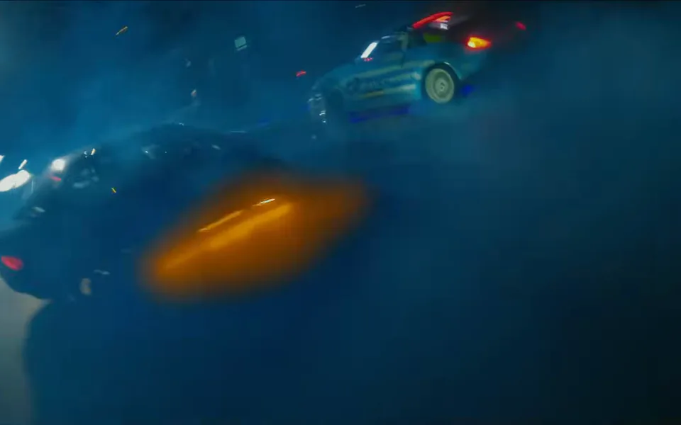 Quadro do anúncio: carros derrapam na fumaça azul em volta de uma luz laranja.