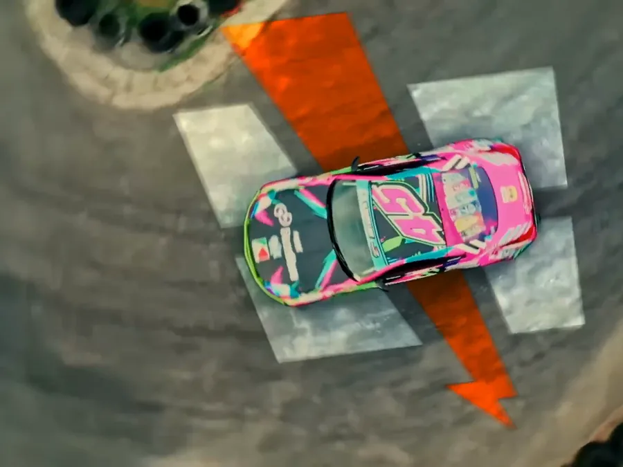 Quadro do filme: o carro visto do alto sobre o raio laranja da Hero Base desenhado no asfalto.
