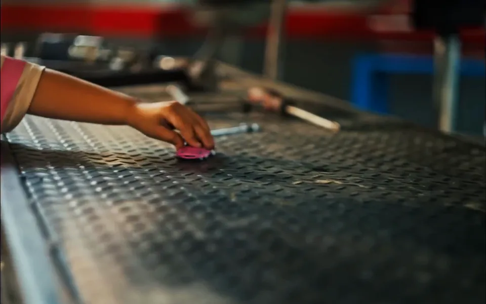 Quadro do filme: um braço de criança coloca um carrinho sobre a bancada de uma oficina.