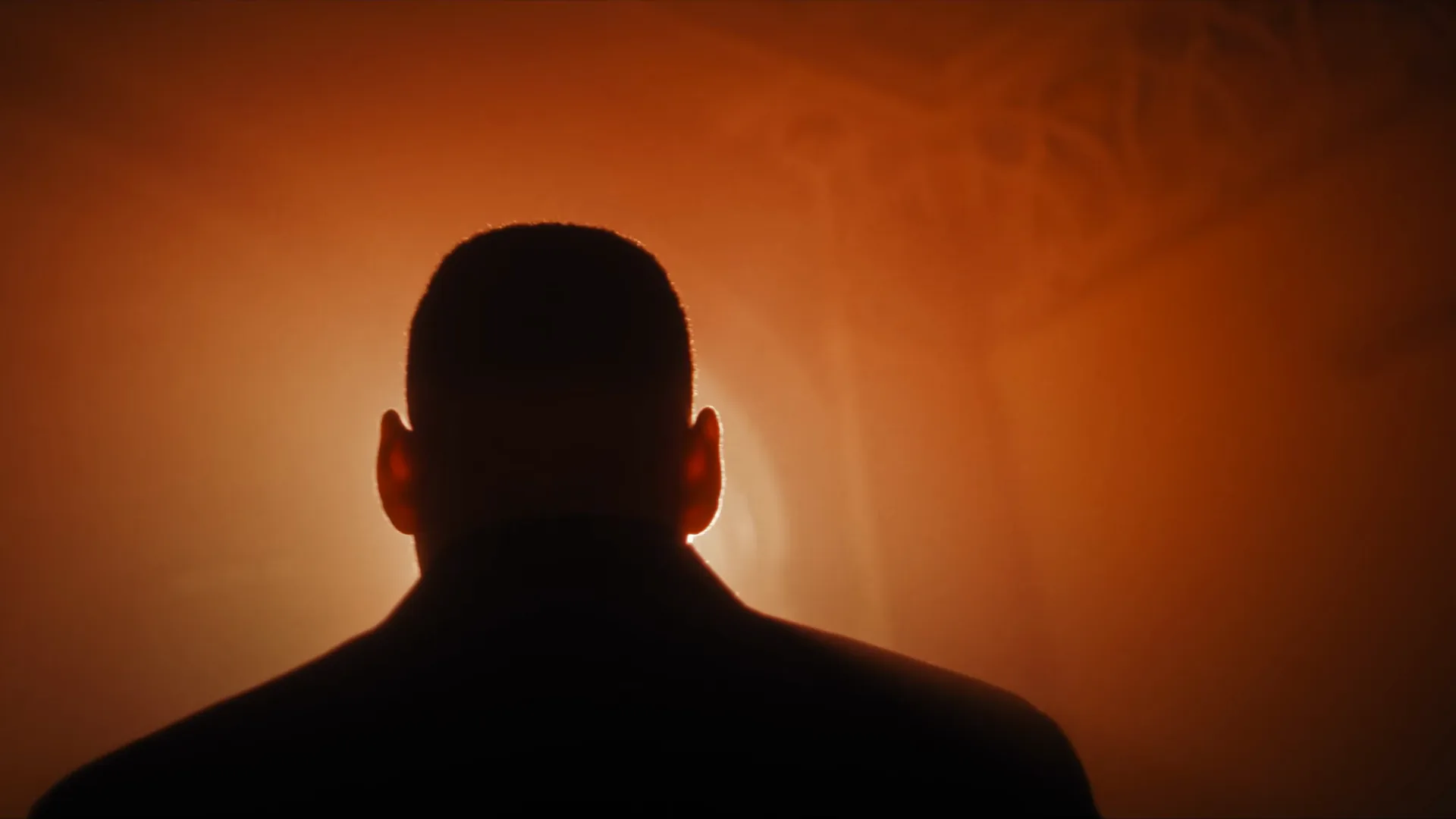 Quadro do filme: um homem de costas, em silhueta, contra uma luz laranja numa sala da mansão.
