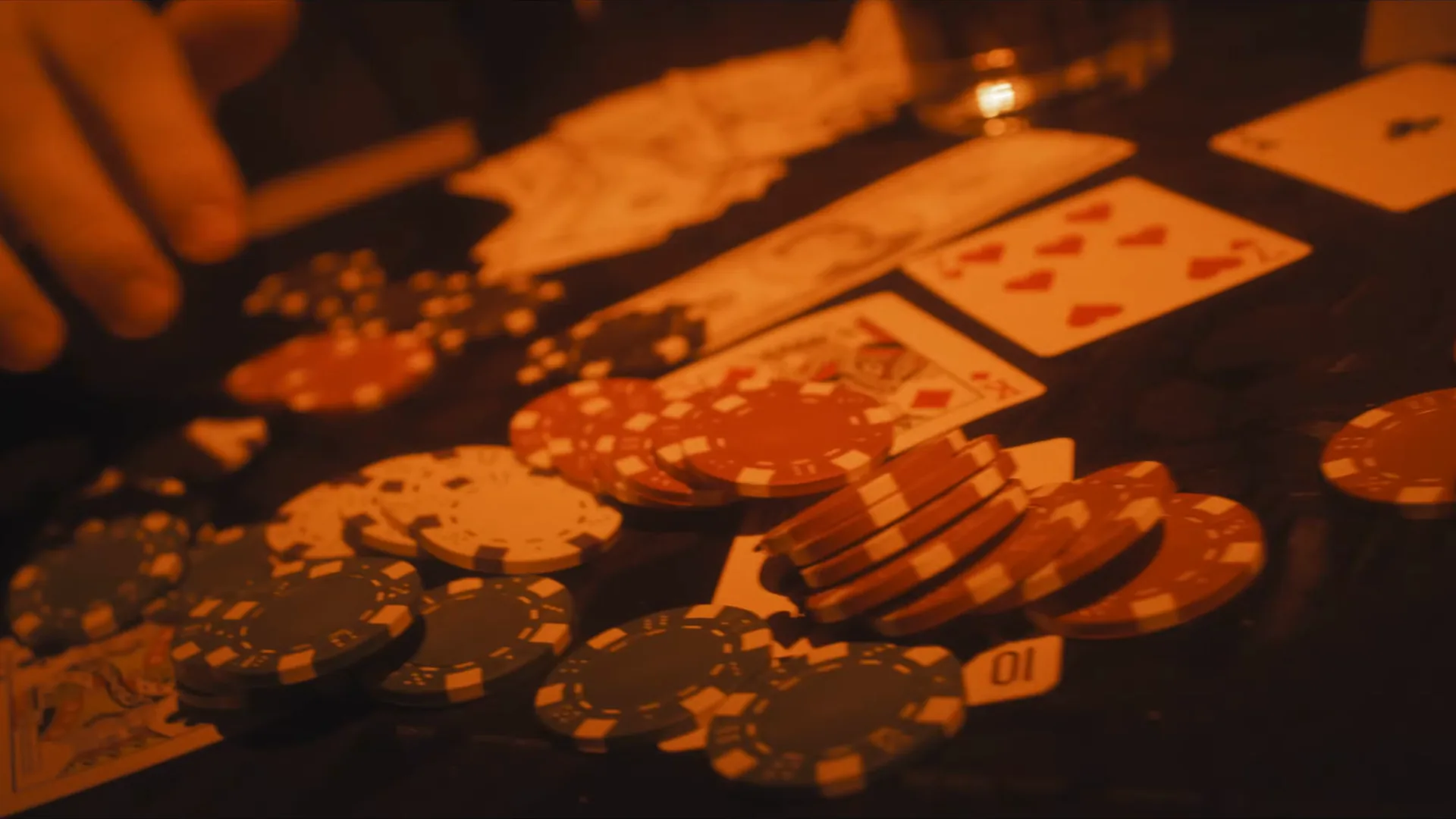 Quadro do filme: fichas e cartas sobre a mesa de pôquer, sob luz laranja.