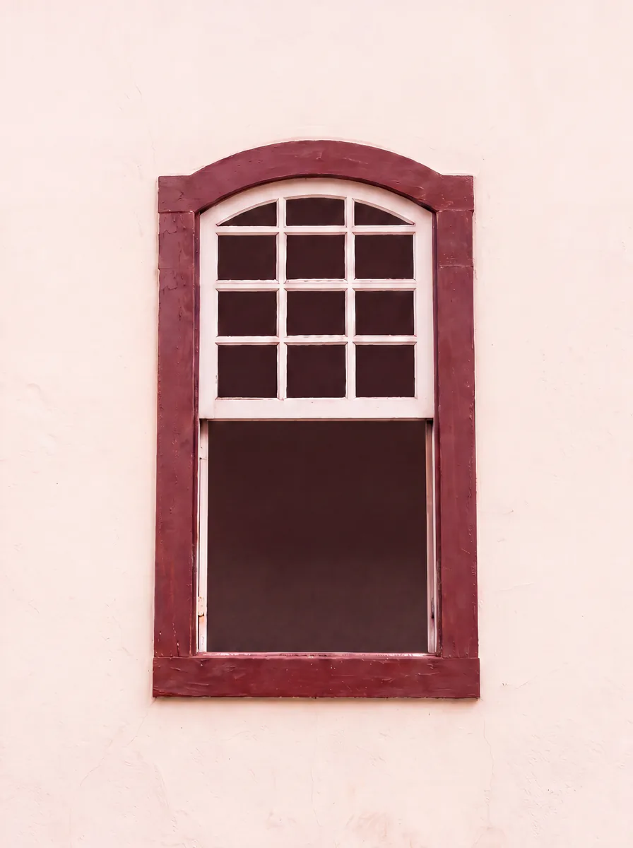 Parede rosada com uma janela colonial vermelha.