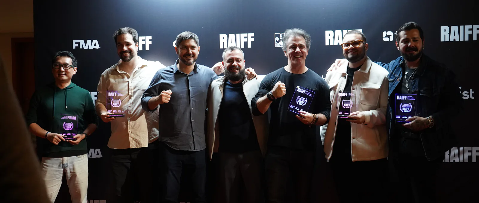 Os premiados do RAIFF 2025 com os troféus diante do painel do festival; o Marco é o segundo da direita, de jaqueta clara.